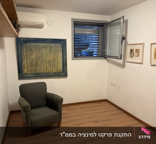 חדר עם רצפת פרקט, כורסה ותמונות על הקיר